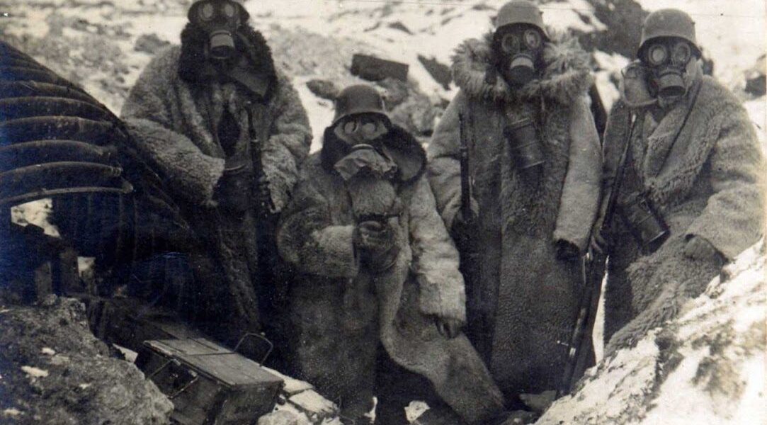 Vier deutsche Soldaten in Pelzmänteln und Gasmasken in einem Schützengraben, 1917