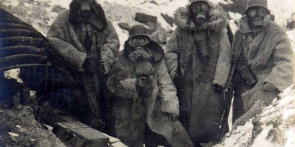 Vier deutsche Soldaten in Pelzmänteln und Gasmasken in einem Schützengraben, 1917