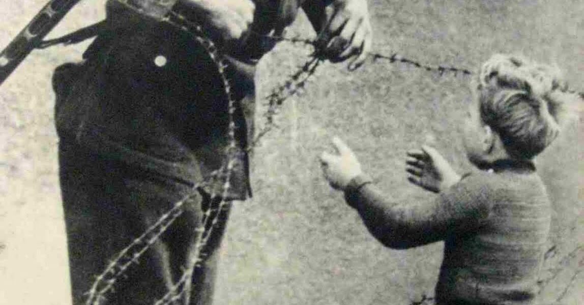 Ostdeutscher Soldat hilft einem kleinen Jungen, über die Berliner Mauer zu schleichen, 1961