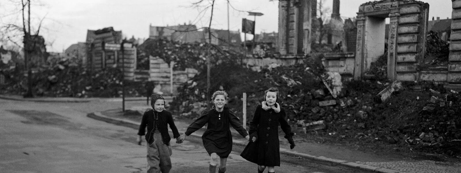 Drei Schülerinnen laufen auf Schlittschuhen von der Schule nach Hause und kommen dabei an zerstörten Häuserblocks in Essen vorbei, 1949