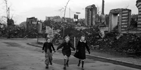 Drei Schülerinnen laufen auf Schlittschuhen von der Schule nach Hause und kommen dabei an zerstörten Häuserblocks in Essen vorbei, 1949