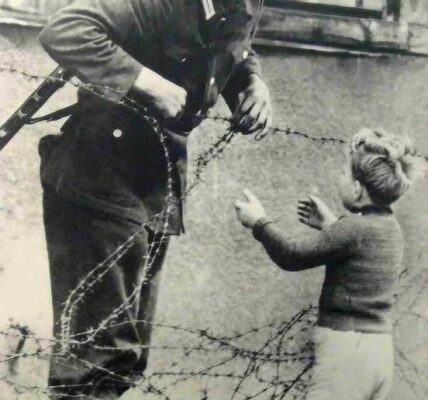 Ostdeutscher Soldat hilft einem kleinen Jungen, über die Berliner Mauer zu schleichen, 1961