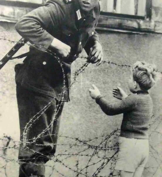 Ostdeutscher Soldat hilft einem kleinen Jungen, über die Berliner Mauer zu schleichen, 1961