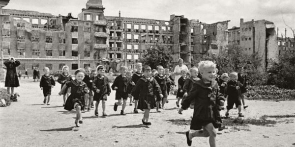 Drei Schulerinnen laufen auf Schlittschuhen von der Schule nach Hause und kommen dabei an zerstörten Häuserblöcken in Essen vorbei, 1949