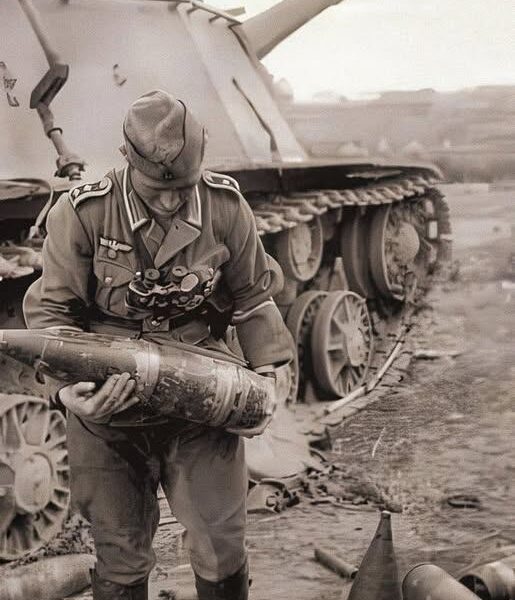 Ein deutscher Feldwebel betrachtet eine erbeutete 152-mm-Granate vor einem zerstörten sowjetischen SU-152 – Ostfront, 1943!