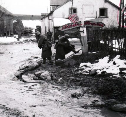 Deutsche Soldaten nehmen toten amerikanischen Soldaten an einer Kreuzung in Belgien Stiefel und andere Ausrustung ab, 1944