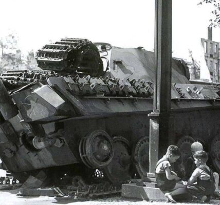 Nachkriegsdeutschland: Kinder spielen vor einem zerstörten deutschen Panzer – ein stilles Zeugnis des Wiederaufbaus.