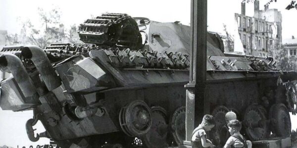 Nachkriegsdeutschland: Kinder spielen vor einem zerstörten deutschen Panzer – ein stilles Zeugnis des Wiederaufbaus.